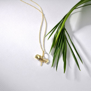 The Faith Hope Love Necklace is a 14K Gold Necklace adorned with a Cross Charm Pendant along with heart and anchor charms, representing faith, hope, and love. Each charm gracefully hangs from a delicate gold chain set against a pristine white background.