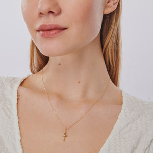 The 14K Gold Tiny Cross Necklace, featuring a small and simple solid yellow gold pendant, is elegantly showcased against a pristine white background. This hypoallergenic jewelry piece combines timeless style with comfort.