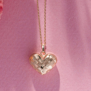 The 14K Gold 3D Puffy Heart Necklace, featuring a minimalist heart pendant with a woven texture, elegantly dangles on a delicate chain against a white background.