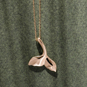 The 14K Gold Whale Mermaid Dolphin Tail Necklace features a pendant shaped like a sleek whale's tail with a polished finish, elegantly suspended from a delicate chain against a white background.