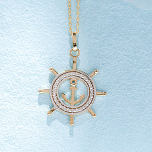 The 14K Gold Ship Wheel and Anchor Necklace is a stunning piece of nautical jewelry, featuring a gold anchor charm at the center of a ship's wheel pendant. The design is elegantly complemented by silver detailing around the anchor, creating a beautiful contrast against the gold finish.