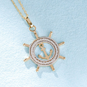 The 14K Gold Ship Wheel and Anchor Necklace is a stunning piece of nautical jewelry, featuring a gold anchor charm at the center of a ship's wheel pendant. The design is elegantly complemented by silver detailing around the anchor, creating a beautiful contrast against the gold finish.