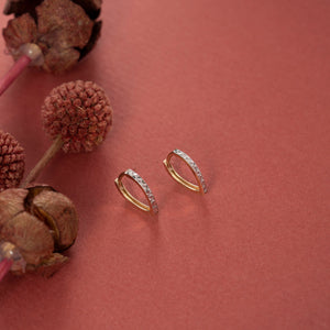 A pair of 14k Solid Gold Small Hoops showcases a distinctive two-tone design. One half features smooth gold, while the other half is adorned with textured silver and a geometric pattern reminiscent of diamond cut earrings. These striking earrings are elegantly displayed against a plain white background.