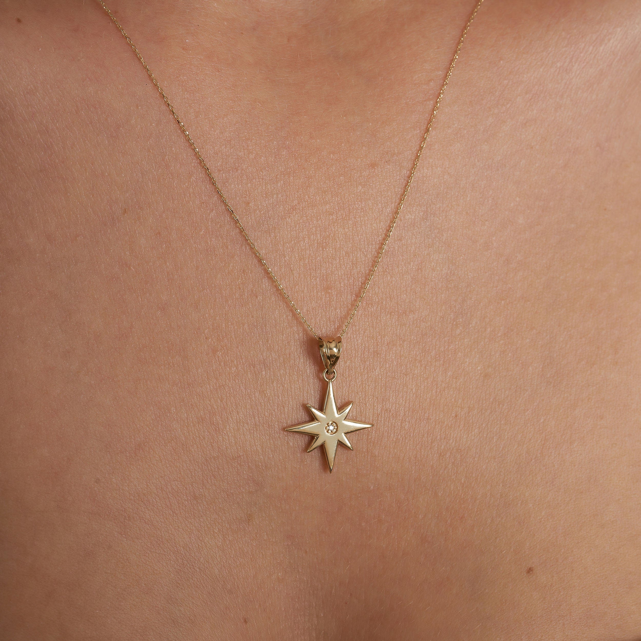 The 14K Gold North Star Pendant Necklace by RundaJewelryUs, featuring a delicate chain and a central gemstone accented pendant, elegantly graces a plain skin backdrop—making it the perfect graduation gift to symbolize guidance and new beginnings.