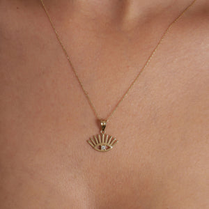 The 14K Solid Gold Evil Eye Necklace showcases a pendant in the shape of an eye, accented with sunburst rays extending above and below. At the center of this elegant design is a small round diamond, all suspended from a delicate gold chain. This piece serves as both a beautiful adornment and a symbol of protection.