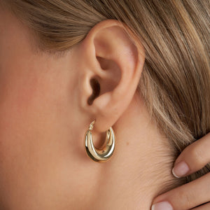 Introducing our 14K Real Gold Thick Hoop Earrings: These elegant earrings showcase a chunky design with a polished gold finish, offering a shiny surface. Crafted from 14k gold, they feature an oval shape with a secure clasp closure. The earrings are beautifully displayed against a plain white background.