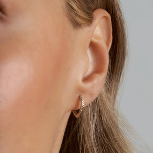 A pair of 14k Solid Gold Small Hoops showcases a distinctive two-tone design. One half features smooth gold, while the other half is adorned with textured silver and a geometric pattern reminiscent of diamond cut earrings. These striking earrings are elegantly displayed against a plain white background.