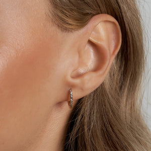 A pair of 14k Solid Gold Small Hoops showcases a distinctive two-tone design. One half features smooth gold, while the other half is adorned with textured silver and a geometric pattern reminiscent of diamond cut earrings. These striking earrings are elegantly displayed against a plain white background.