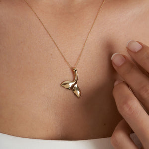 The 14K Gold Whale Mermaid Dolphin Tail Necklace features a pendant shaped like a sleek whale's tail with a polished finish, elegantly suspended from a delicate chain against a white background.