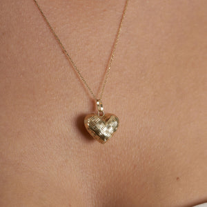 The 14K Gold 3D Puffy Heart Necklace, featuring a minimalist heart pendant with a woven texture, elegantly dangles on a delicate chain against a white background.