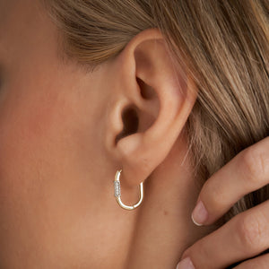 The 14k Solid Gold Oval Small Hoops by RundaJewelryUs are delicately designed with rectangular sections adorned with small diamonds, making them ideal as cartilage earrings. Their luxurious charm enhances any outfit, and they are beautifully presented against a white background.