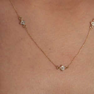 A refined 14K gold necklace adorned with evenly spaced, small flower-shaped diamond pendants along the chain, elegantly showcased on a white background.