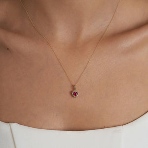 The 14K Gold Heart Ruby Necklace showcases a delicate gold chain paired with a captivating ruby heart pendant, embellished with smaller white stones that enhance its sparkle. This elegant and lightweight necklace is a beautiful accessory designed for women.