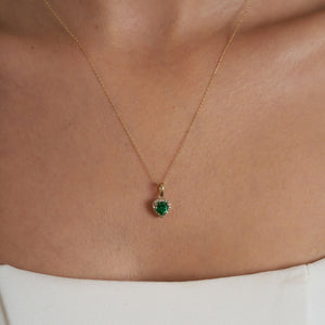 The 14K Gold Heart Emerald Necklace showcases a green, heart-shaped zirconia emerald pendant elegantly surrounded by small, sparkling diamonds, forming a delicate and luxurious necklace for women.