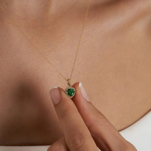 The 14K Gold Heart Emerald Necklace showcases a green, heart-shaped zirconia emerald pendant elegantly surrounded by small, sparkling diamonds, forming a delicate and luxurious necklace for women.