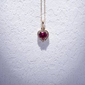 The 14K Gold Heart Ruby Necklace showcases a delicate gold chain paired with a captivating ruby heart pendant, embellished with smaller white stones that enhance its sparkle. This elegant and lightweight necklace is a beautiful accessory designed for women.