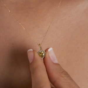 Introducing the 14K Gold Heart Shaped Citrine Necklace for women, featuring a central yellow citrine gemstone beautifully encircled by a halo of petite white diamonds, elegantly set against a simple light backdrop.