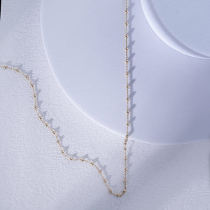 Introducing the 14K Gold Station Minimal Chain Necklace, showcasing a delicate chain adorned with small, evenly spaced beads against a plain white backdrop. This sophisticated piece is equipped with a simple clasp at the top center, making it ideal for layering with other jewelry.