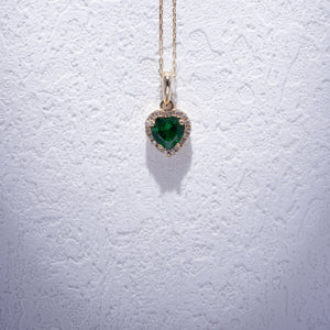 The 14K Gold Heart Emerald Necklace showcases a green, heart-shaped zirconia emerald pendant elegantly surrounded by small, sparkling diamonds, forming a delicate and luxurious necklace for women.