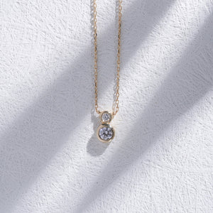 The 14K Gold Zirconia Necklace showcases two round diamond pendants on a delicate chain, arranged vertically with the larger pendant positioned below the smaller one. The white background enhances the necklace's elegance, making it an ideal piece of dainty gold jewelry for bridal occasions.