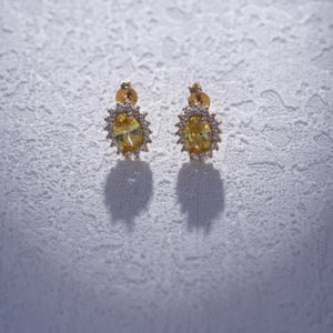 The 14K Solid Gold Oval Shaped Citrine Stud Earrings display vintage citrine gemstones, each set in a halo of small white diamonds. They feature a screw-back design and are presented against a plain white background.