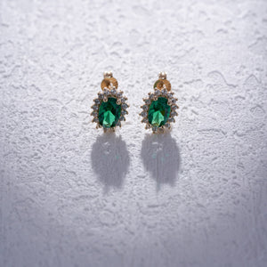 Introducing the 14K Gold Oval Shaped Stud Emerald Earrings, adorned with vintage oval-cut green gemstones and bordered by delicate round white diamonds. These earrings boast a polished finish and are secured with a post and butterfly back fastening.