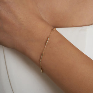 Introducing the 14K Gold Minimal Station Bracelet by RundaJewelryUs: a delicate design featuring a thin chain accented with small, evenly spaced tube-shaped beads in lustrous 14K gold. This elegant piece is securely fastened with a traditional lobster claw closure.