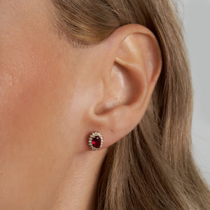 Introducing the 14K Gold Oval Shaped Ruby Stud Earrings, featuring stunning red gemstones encased in 14K gold and surrounded by a halo of sparkling white diamonds, perfect for adding a touch of elegance.