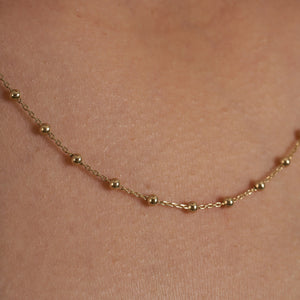 Introducing the 14K Gold Station Minimal Chain Necklace, showcasing a delicate chain adorned with small, evenly spaced beads against a plain white backdrop. This sophisticated piece is equipped with a simple clasp at the top center, making it ideal for layering with other jewelry.