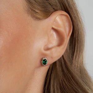 Introducing the 14K Gold Oval Shaped Stud Emerald Earrings, adorned with vintage oval-cut green gemstones and bordered by delicate round white diamonds. These earrings boast a polished finish and are secured with a post and butterfly back fastening.