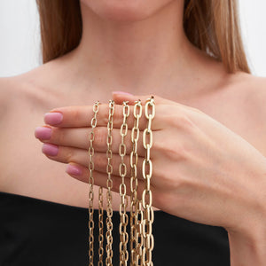 A collection of gold chains, highlighted by the exquisite 14K Gold Paperclip Chain Necklace, is arranged in a semi-circle. Each piece showcases distinct link sizes and styles characteristic of Italian design jewelry. They are layered from smallest to largest, creating a cascading effect against the white background.