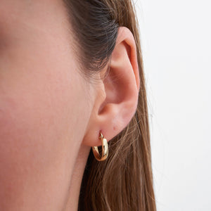 A pair of 14K Gold Round Hoop Earrings displayed on a plain white background features one earring shown from the side, showcasing its sleek, modern round shape and smooth finish, while the other is presented from the front, emphasizing its lightweight clasp mechanism.