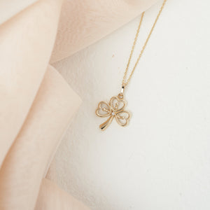 The 14K Gold Clover Pendant Necklace boasts heart-shaped leaves and a central Cubic Zirconia gemstone, with a delicate chain enhancing the gold hue for an exquisite accessory.