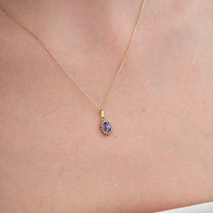 Product Description: The 14K Gold Amethyst Necklace features an oval-shaped amethyst pendant encircled by a halo of shimmering zirconia stones. Its elegant design is mesmerizing, set against a pure white backdrop.