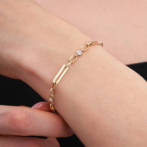 The 14K Gold Paperclip Link Chain Bracelet is a refined piece crafted from solid gold, showcasing an elegant design that alternates between elongated paperclip links and small circular links. It is embellished with three evenly spaced, small round diamonds along the chain, making it perfect for layering. The bracelet secures with a lobster clasp.