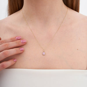 The 14K Gold Oval Cubic Zirconia Gemstone Necklace showcases a delicate design with an oval-shaped pendant adorned with a prominent cubic zirconia gemstone. Smaller stones encircle the centerpiece, creating a dazzling effect against a simple white backdrop.