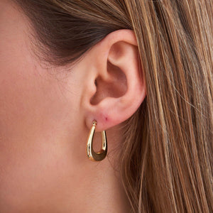 Presenting the 14K Gold Thick Hoop Earrings, these pieces boast a modern, slightly tapered design in yellow gold. Set against a plain white backdrop, one earring is displayed face-on while the other is shown from a side angle to highlight their shiny and smooth finish. Ideal for those in search of hypoallergenic jewelry.