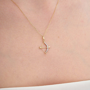 The Love Minimal Gold Arrow Necklace is crafted from 14k gold and showcases a bow charm pendant elegantly adorned with small diamonds along its curve. Its thin and delicate chain ensures a touch of elegance, while the hypoallergenic material guarantees comfort for sensitive skin.