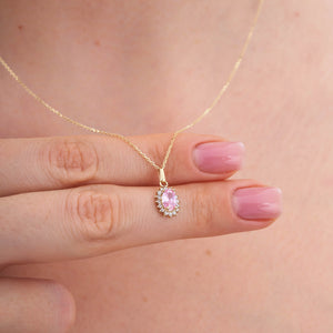 The 14K Gold Rose Quartz Necklace features an oval-shaped pendant with a stunning pink rose quartz gemstone, surrounded by a halo of small white diamonds. Its delicate chain elegantly contrasts with the vibrant stones, symbolizing healing relationships and exuding sophistication.