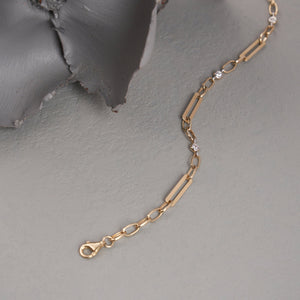 The 14K Gold Paperclip Link Chain Bracelet is a refined piece crafted from solid gold, showcasing an elegant design that alternates between elongated paperclip links and small circular links. It is embellished with three evenly spaced, small round diamonds along the chain, making it perfect for layering. The bracelet secures with a lobster clasp.