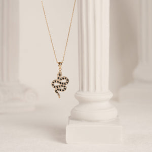 The 14K Solid Gold Snake Necklace features a pendant that beautifully resembles a coiled serpent with intricate black spots. This elegant charm is suspended from a fine chain, set against a plain white background, creating an outstanding piece of jewelry.