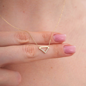 The 14K Gold Triangle Symbol Pendant Necklace by RundaJewelryUs features a triangle charm adorned with a row of small, sparkling diamonds on one side. The delicate chain enhances the minimalistic and elegant design of the centrally hanging pendant.