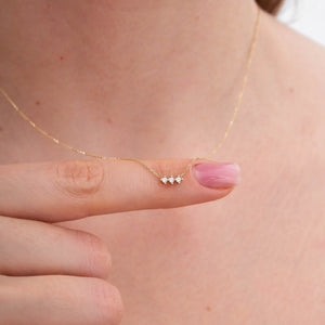 The 14K Gold Trio Necklace is a delicate piece with three small, round diamond stones set in a row on a thin, hypoallergenic gold chain against a light background.