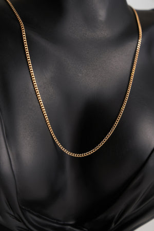 The 14K Solid Gold Curb Cuban Link Chain is a delicately crafted necklace made from real 14K gold, highlighting a simple and elegant design against a white background. This hypoallergenic piece features small interlocking links that form a continuous loop, making it perfectly unisex for any wearer.