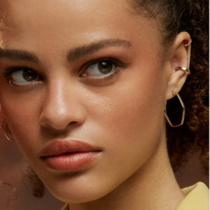 The 14K Gold Hexagon Hoop Earrings from the Harmony Collection by RundaJewelryUs feature an eye-catching geometric design. The left earring boasts a slightly irregular hexagonal shape, adding a modern touch to your everyday style, while the right one is viewed from the side, highlighting its thin profile and smooth, shiny finish.