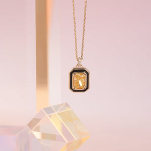 The 14K Gold Citrine Necklace showcases a rectangular yellow gemstone pendant, elegantly framed in black and adorned with small white stones. Its delicate chain enhances the vibrant centerpiece perfectly.