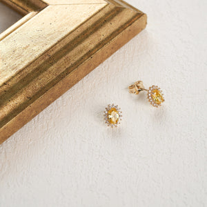 The 14K Solid Gold Oval Shaped Citrine Stud Earrings display vintage citrine gemstones, each set in a halo of small white diamonds. They feature a screw-back design and are presented against a plain white background.