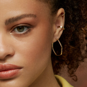 The 14K Gold Hexagon Hoop Earrings from the Harmony Collection by RundaJewelryUs feature an eye-catching geometric design. The left earring boasts a slightly irregular hexagonal shape, adding a modern touch to your everyday style, while the right one is viewed from the side, highlighting its thin profile and smooth, shiny finish.