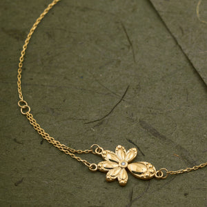 The 14K Solid Gold Diamond Leaf Bracelet from the Chloris Collection showcases a delicate chain link design with a captivating floral charm at its center, making it an ideal bridesmaids' gift for a forest wedding. The simple spring ring clasp and small circular tag provide an elegant touch against the plain white background.