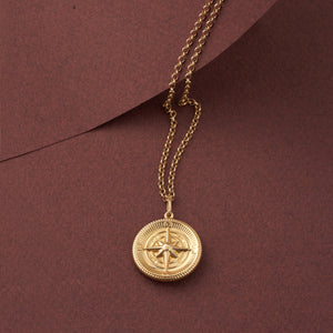 The 14K Solid Gold Compass Necklace for Men showcases a circular pendant with a raised compass design, crafted from solid gold. Its textured edges and polished finish add elegance, while it gracefully hangs on a delicate chain.